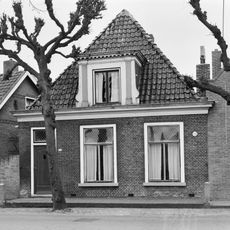 Eenvoudig pand zonder verdieping onder zadeldak met voorschild en grote dakkapel met bloklijst en pilasters