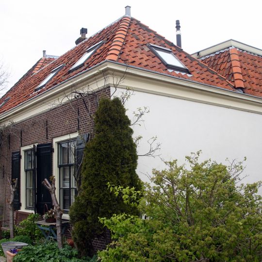 Pand zonder verdieping op L-vormige plattegrond, onder met pannen gedekt zadeldak met schild en wolfeind boven ingezwenkte