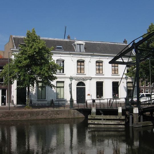 Pand onder zadeldak met gepleisterde lijstgevel met stucversiering. Stoeppalen. Vormt een geheel met het buurnummer 97