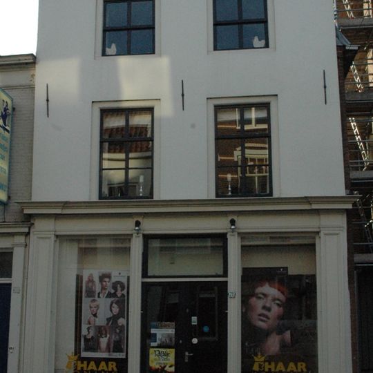 Hoekpand . Pand met schilddak, aan de achterzijde afgesloten door een puntgevel. Gepleisterde lijstgevel met schuiframen in de verdiepingen. Zijgevel modern