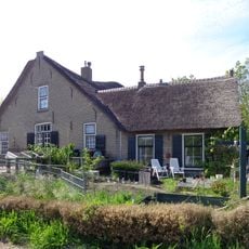 Gedeelte van een boerderij, waarvan de verschillende onderdelen een schilderachtig geheel vormen. Hoge stal onder zadeldak met riet gedekt