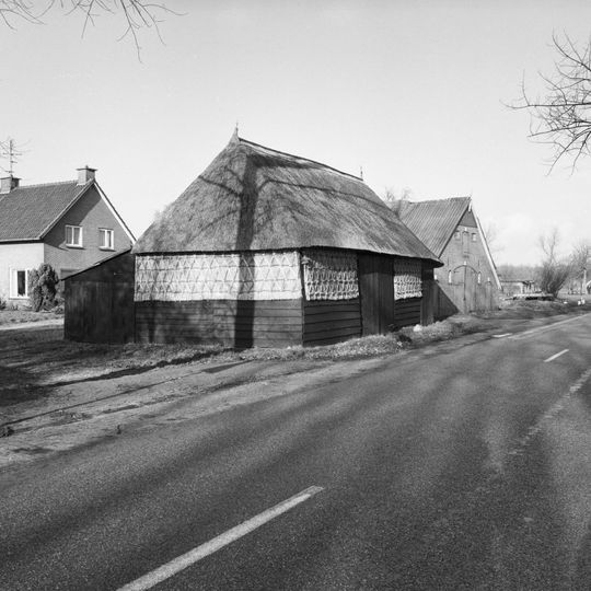 Bij het leegstaande boerderijtje Rheezerweg 95 langs de weg een schuurtje met wanden van stro en hout onder rieten schilddak