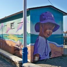 El mural representa a una niña de medio cuerpo y de perfil con camiseta y gorro playero de color morado.