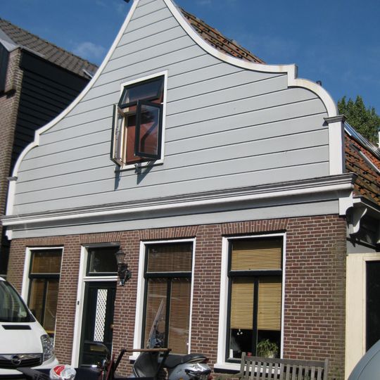 Houten dijkhuis met klokgevel uit 19de eeuw, bakstenen onderpui