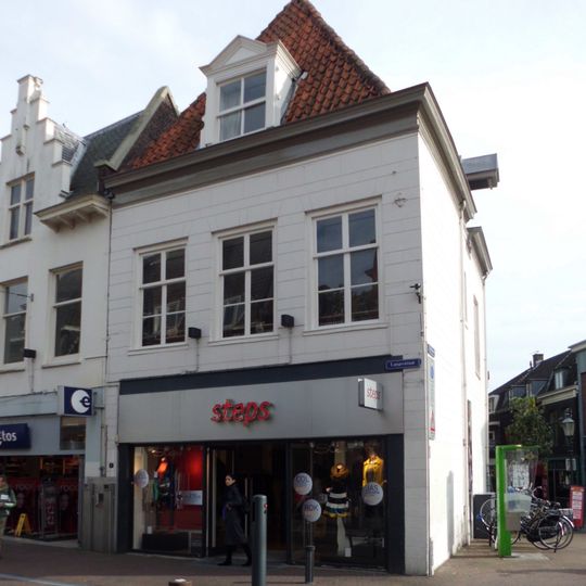 Pand met hoog tentdak, door winkel aangetast. Aan achterzijde en zijkant oude staat het beste afleesbaar