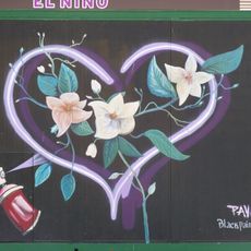 Mural que representa unas ramas con flores enmarcadas en un corazón de neón junto a un bote de espray sobre fondo negro.