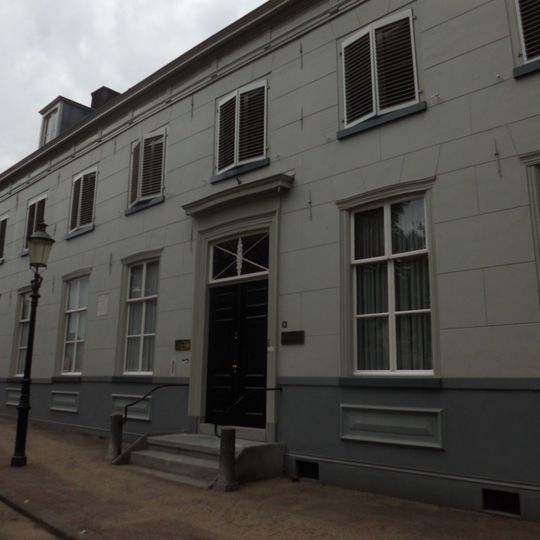 Gepleisterde brede gevel, woonhuis van een 19e-eeuws karakter, ouder huis aanwezig. Rechte kroonlijst