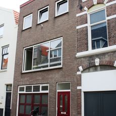 Huis met 19e-eeuwse bepleisterde lijstgevel. Fraaie kap. Nok evenwijdig aan de straat. Dakkapel. Getoogde vensters