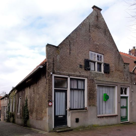 Pand met IJsselstenen puntgevel, voorzien van vlechtingen en geprofileerde dekplaten opzij en op de top. Kruiskozijnen en luiken