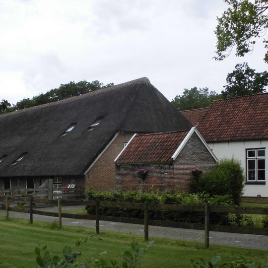 Boerderij bestaande uit een schuur onder rieten wolfdak, waarvoor een woonhuis is aangebouwd met gepleisterde wanden, een ingezwenkt lijstgeveltje en een met pannen gedekt dak, alsmede het bakhuis