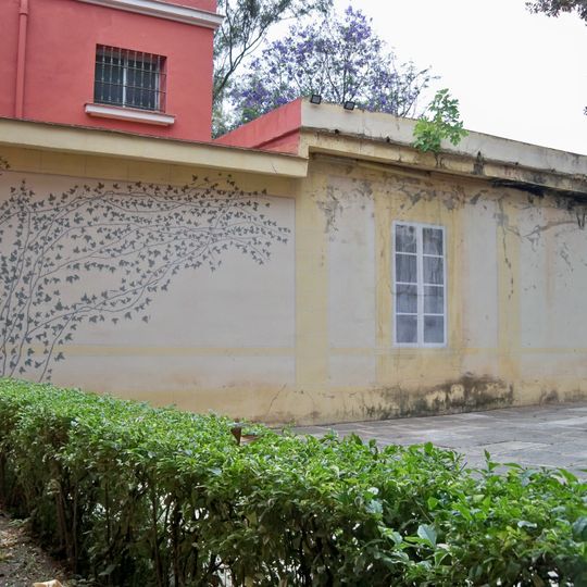 Mural en un edificio anexo a la Hacienda Nadales que representa una planta trepadora que parece surgir del seto y unas ventanas que imitan las ventanas de la Hacienda San José que se encuentra junto al edificio de la Hacienda Nadales.