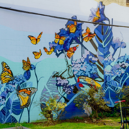 This 20--by-25 feet mural was inspired by Robert G. Ingersoll’s quote, “We Rise by Lifting Others” includes a scene of a migration of monarch butterflies using vibrant purples and blues atook about ten days to complete.
