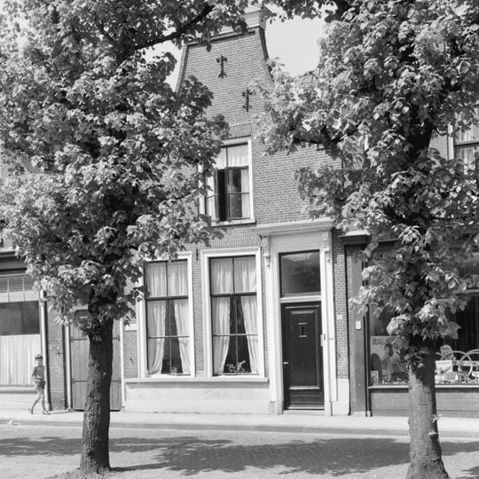 Woonhuis onder zadeldak tegen halsgevel met aanzetkrullen en bekroond door fronton