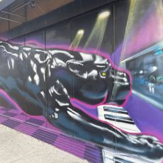 A mural depicting a panther playing a keyboard while looking out a window. The mural heavily features tones of purple, including a checkered floor alternating between light and dark purple.