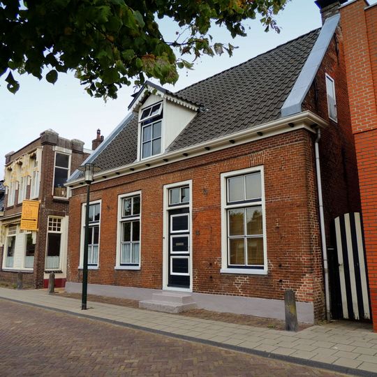 Pand onder zadeldak evenwijdig aan de straat tussen topgevels waarin sierankers en half kruiskozijn