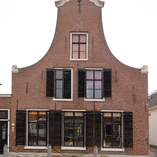 Pand met verdieping en vlieringverdieping onder zadeldak tegen slanke klokgevel met aanzetkrullen en gebeeldhouwde kuiflijst