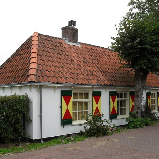 Gepleisterd pand zonder verdieping onder hoog met pannen gedekt schilddak. Twee vensters met negenruitsschuiframen in de voorgevel