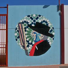 Mural que representa el busto de perfil de un hombre ataviado con sombrero y elementos de la fiesta de verdiales sobre un fondo geométrico.
