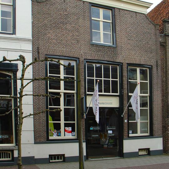 Huis met lijstgevel met ingezwenkte zijkanten en met schuiframen en winkel-ingangspartij uit de bouwtijd