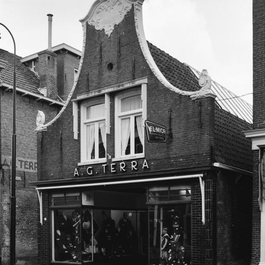 Pand onder zadeldak tegen klokgevel met gebeeldhouwde lijsten en aanzetkrullen en beeldhouwwerd in de top