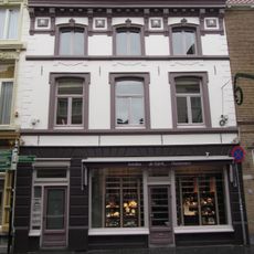 Huis met witgepleisterde en van stucversiering voorziene lijstgevel en hoog met rode pannen belegd zadeldak