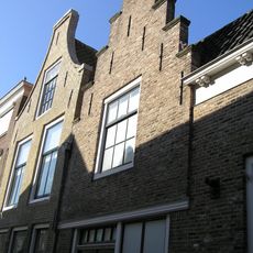 Aansluitend bij Poststraat 1 een aanbouw met lijstgevel en vervolgens een aanbouw met langsgevel aan de straat en ten slotte een trapgevel met geprofileerde dekstukken, puibalk.