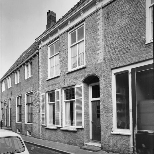 Fors L-vormig pand onder schilddak met gepleisterde rechte gevels. Kroonlijst met klossen. Schuifvensters