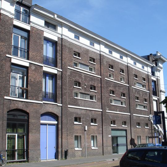 Onderdeel van een reeks pakhuizen. Lijstgevel met getoogde vensters en cordonlijsten