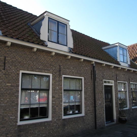 Pand onder zadeldak, evenwijdig aan de straat. In de 19e eeuw samengetrokken uit twee woningen. Dakkapellen met vleugelstukken.