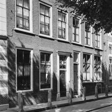 Pand met lijstgevel aan de straat, voordeuromlijsting met bovenlicht en verdiepte panelen in de zijposten, 6-ruits schuifvensters met rode strekken en rode beneden rollaag.