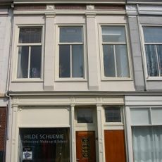 Pand met verminkte bakstenen gevel met rechte kroonlijst. De verdieping voorzien van Dorische pilasterstellingen en fries van metselmozaïek