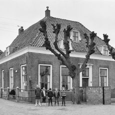 Op de hoek van de Westdijk gelegen pand zonder verdieping onder omlopend pannen schilddak, waarin dakvensters met zijstukken.
