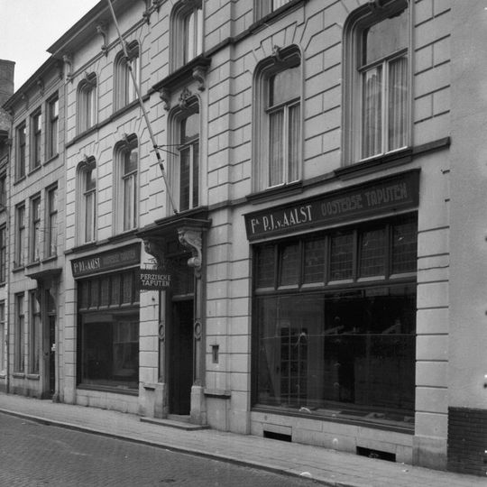 Huis met gebosseerd gepleisterde lijstgevel, waarin vensters met afgeronde bovenhoeken, kuiven van stuc en voluutvormige consoles onder de kroonlijst