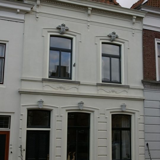 Huis onder schilddak en met grijsgepleisterde lijstgevel, waarin segmentvormig overtoogde vensters met kuiven in stucwerk