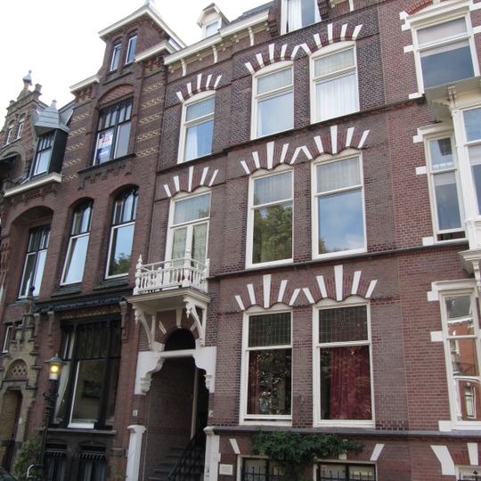 Pand in neo-renaissance trant. Souterrain. Gevelversiering met geblokte vensterstrekken en gekoppelde ontlastingsboogjes. Boven de ingang een houten balcon