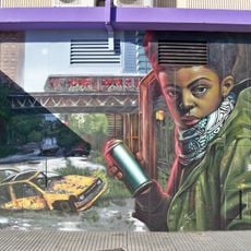 Mural que representa a un grafitero con un bote de pintura en espray en la mano sobre un paisaje urbano de fondo donde se ven los restos de un coche abandonado y un tranvía elevado en cuyos vagones se lee «Nesui» y «Lalone».