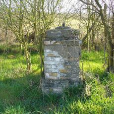 Podstavec s ulomeným kovovým křížem u silnice z Malíče