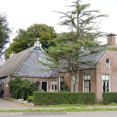 Kop-hals-rompboerderij met topgevels met zesruitsvensters, lijsten met boeiborden en topschoorstenen met borden