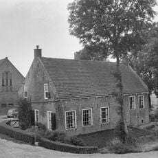 Boerderij waarvan alleen de afzonderlijke woning van belang is, met zadeldak tussen zijtopgevels, in de gevel nog sporen van de oorspronkelijke vensters met korfbogen waarin natuursteenblokjes