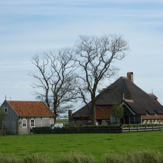 Ver van de weg richting Waddendijk gelegen en door bomen omsingelde stolphoeve met lang voorhuis waarvan de topgevel een houten voorschot heeft