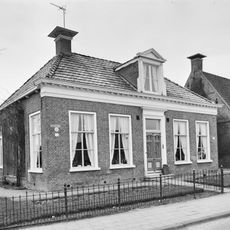 Woonhuis met zesruitsvensters en geblokte kroonlijst onder laag schilddak met dakkapel en hoekschoorstenen met borden