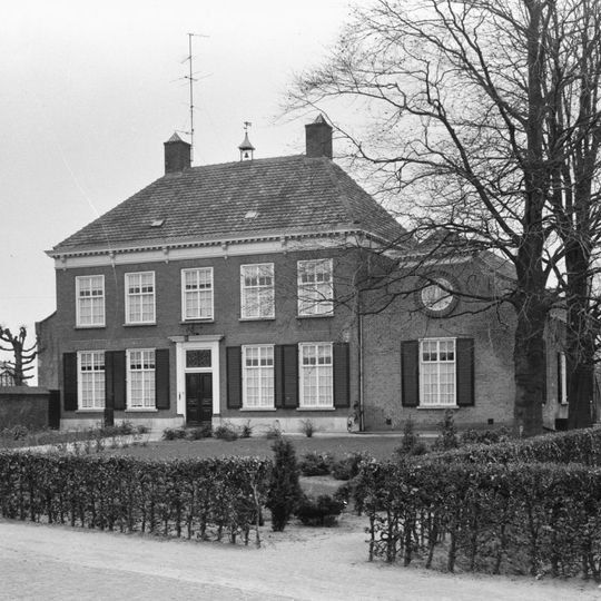 Herenhuis onder dwars schilddak met hoekschoorstenen, kroonlijst op klossen en voluutvormige consoles, ramen met kleine roedenverdeling, pilasters en kroonlijst om de