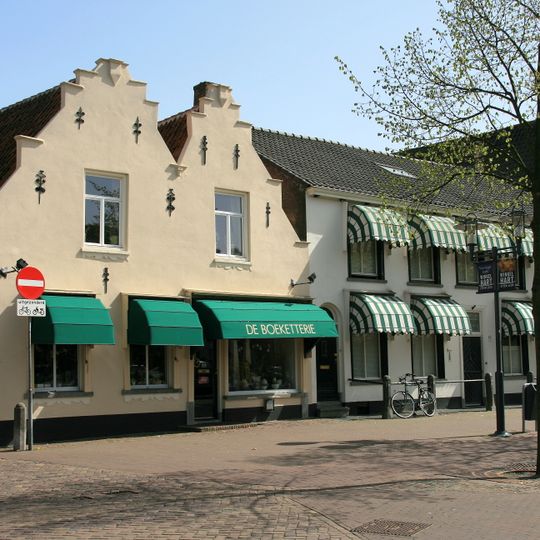 Huis met eeuwse tweeling-trapgevel, waarin een met een masker versierd jonisch kraagsteentje en tien eenvoudige sierankers, venster vergroot en rechts beganegronds een etalagevenster uitgebroken