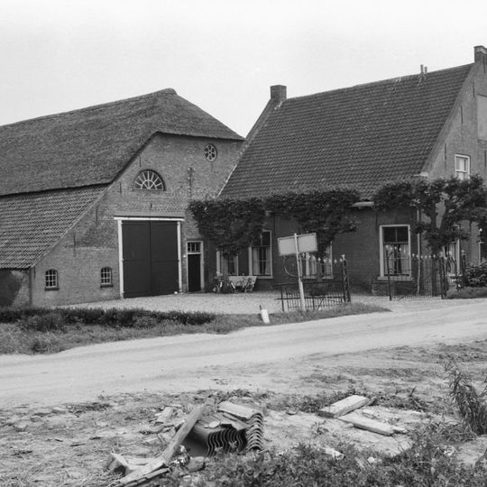 Grote hoeve, waarvan het woongedeelte een puntgevel met rollaag heeft. Geprofileerde zijdekplaten en in de top een jaartal. In de voorgevel vensters met zesruitsschuiframen.