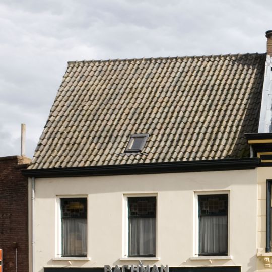 Eenvoudig huis, beneden geheel verbouwd voor winkel, gepleisterde lijstgevel, dwars zadeldak en zijtopgevels met vlechtingen