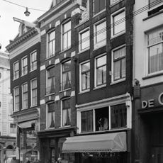 Hoekhuis met voorgevel onder rechte lijst met dakkapel afgeronde pui waarboven nis op de hoek