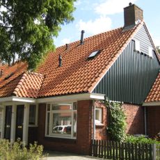 Blok met 8 woningen, gecombineerde toegangen van twee woningen onder een ingestoken schilddak, zijkant met houten topgevel, aan westkant toegangspoort tot binnenterrein.