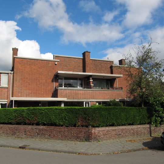 Twee geschakelde herenhuizen die onder een hoek van 45 graden ten opzichte van de rechthoekige kruising liggen, bestaande uit twee bouwlagen onder platte daken