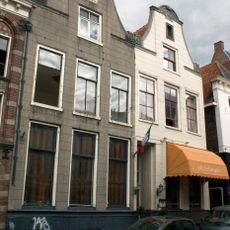 Dubbel pand met twee identieke gepleisterde halsgevels met gebeeldhouwde halfronde topafdekking en aanzetvoluten