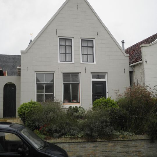 Pand met gepleisterde puntgevel en oude kozijnen met spiegelglas onder zadeldak